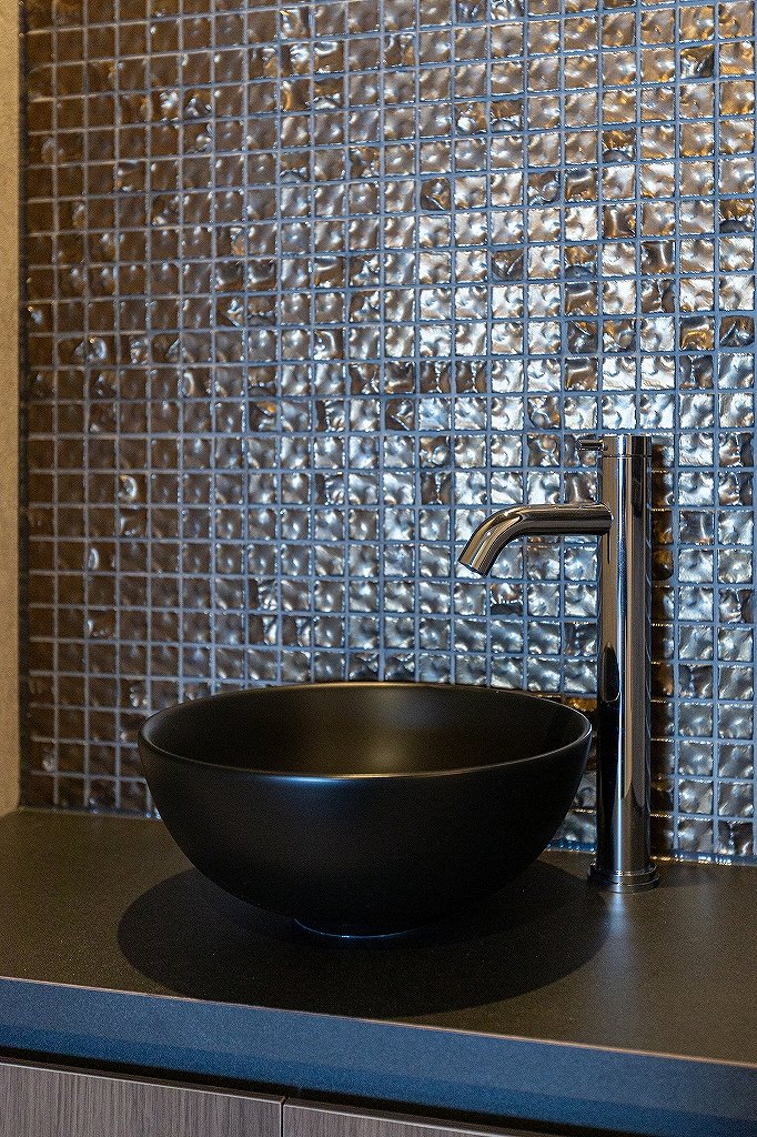 リノベーション後:造作手洗いカウンターとタイルを照らす照明のあるトイレ