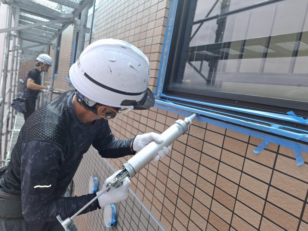 外壁タイル補修工事の施工中の様子:窓枠のコーキング補修作業を行っている場面