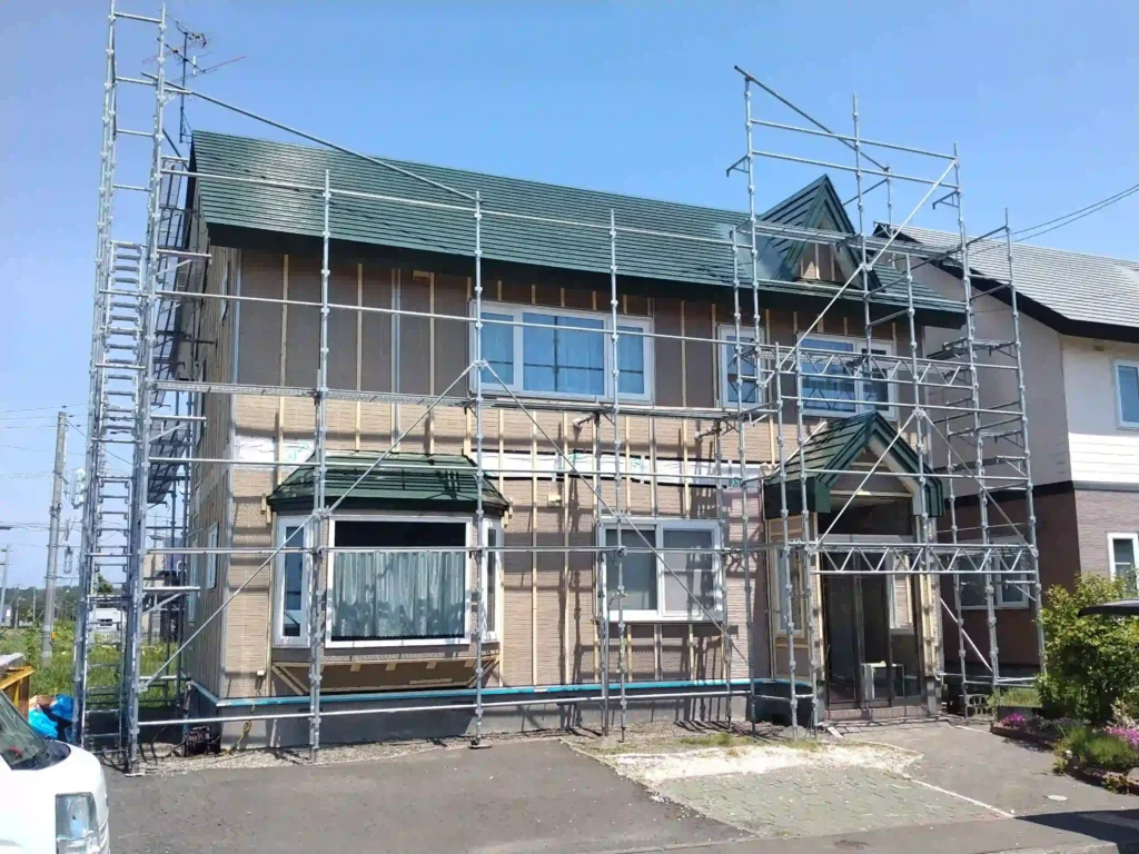 施工中：既存外壁の上から金属サイディングを重ね張りする作業風景