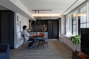 リノベーション後：ダイニングとグレーでまとめたキッチン。ダイニングテーブルに旦那様、キッチンに奥様が立ち会話をしている。