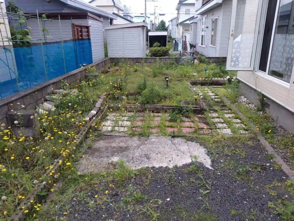 リフォーム前：雑草と荒れたアスファルトが広がる庭の状態